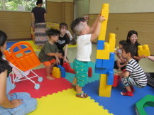 カラフルなマットの上で一人の男の子が黄色と青のブロックを自分の身長より高く積み上げている写真