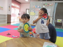 テーブルの前で2人の子どもがシールを貼った手作りのスイカを持ちカメラに笑顔を向けている写真