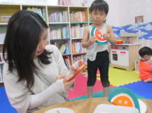 完成した工作品を子どもが両手で持ち、その手前で保護者が携帯で撮影をしようとしている写真