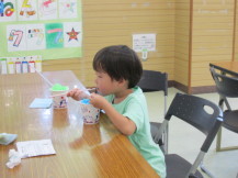 テーブルの前に座り、カップに入ったかき氷を食べている子どもの写真