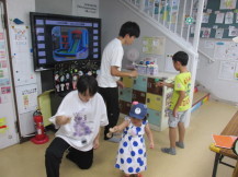 乳幼児の女の子と小学生ぐらいの男の子にそれぞれついてけん玉を教えているような様子の関係者2名の写真