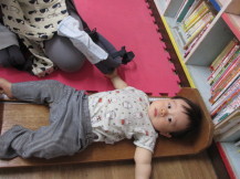 本棚の近くに用意された木の板の上で乳児の身長を測っている写真