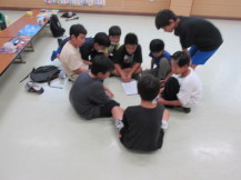 輪になるように床に座って対戦の組み合わせの話をする子どもたちの写真