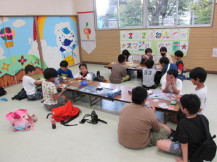 複数のテーブルの前に座ってカードゲームをする大勢の子どもたちの写真