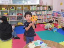 シールを貼ったオレンジ色の紙のかぼちゃを手に持って見せている男の子の写真