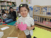 シールを貼ったピンク色の紙のかぼちゃを両手で持って笑っている女の子の写真