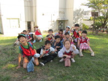 緑の芝生の上に座って集合写真を撮る子どもたちの写真