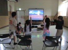 正面のモニターに映し出された映像を見ながら身体を動かして遊んでいる子供達を後方から写した写真