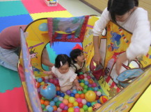 沢山のカラフルなボールが入ったボールプールの中で、楽しく遊んでいる2名の幼児と、その様子を見ている女性の写真