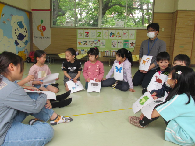 生き物の絵を持った子どもたちが輪になって座っている写真