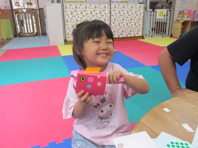 部屋の中でピンク色の服を着た子どもが、自分で作成したこいのぼりの口を動かしている写真