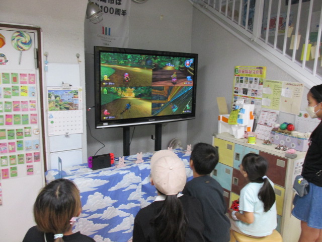 大きいテレビを前に子どもたち4人が椅子に座り、レースゲームをしている写真