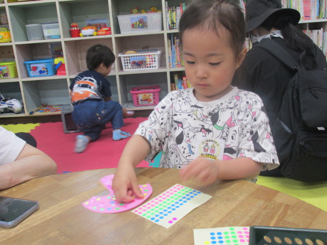 丸い木のテーブルに置かれた傘でデザインされた紙にシールを貼っていく女の子の写真