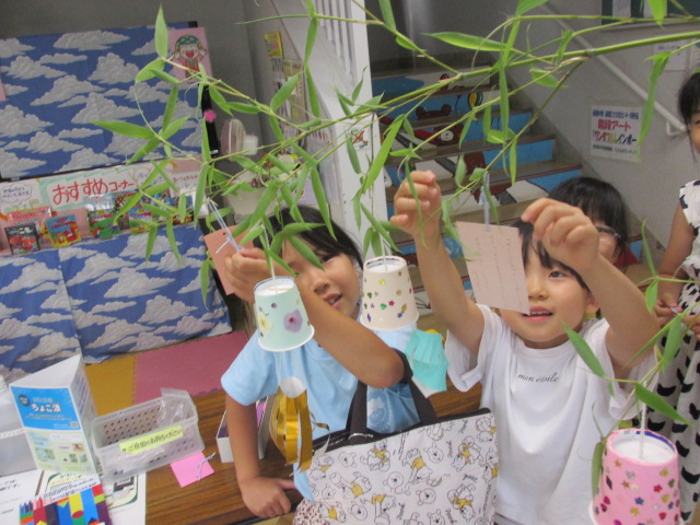 七夕飾りに小学生が短冊を吊るしている写真