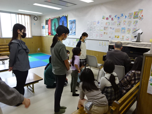 「幸ハッピーベルクラブ」、講師からピアノを使ってベルの音階の説明を受けている子どもたちの写真。