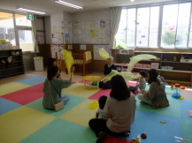 カラーマットの敷かれた部屋で、元保育士の方と一緒に布を宙に舞わせて赤ちゃんを抱っこしてあやしている保護者の方たちの写真