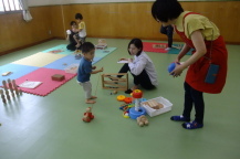 おもちゃに夢中になって遊ぶ男の子と見守る母親と講師の写真