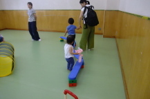 平均台を手を繋いで歩く親子たちの後ろ姿を撮影している写真