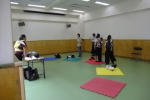 講師のおんぶのやり方を真剣に聞いている母親たちを撮影している写真