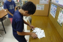長テーブルに置かれた沢山の洗濯ばさみの前に立っている子どもの写真