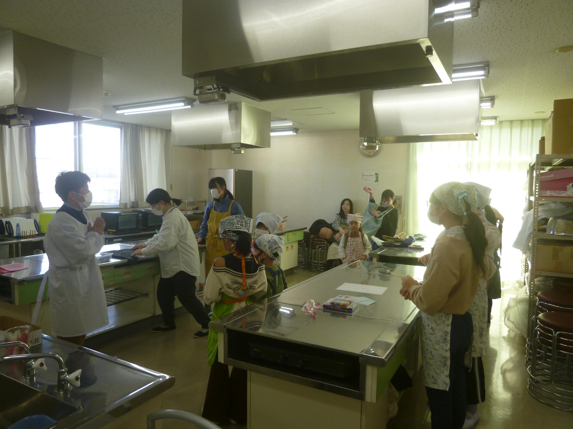 老人福祉センター調理室で調理工程の説明を受けている参加者の写真