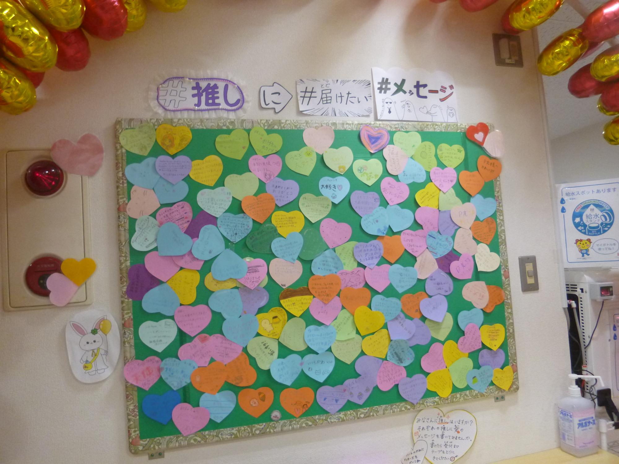 推しへのメッセージが書かれたハート型のメッセージカードが貼られた掲示板の写真。