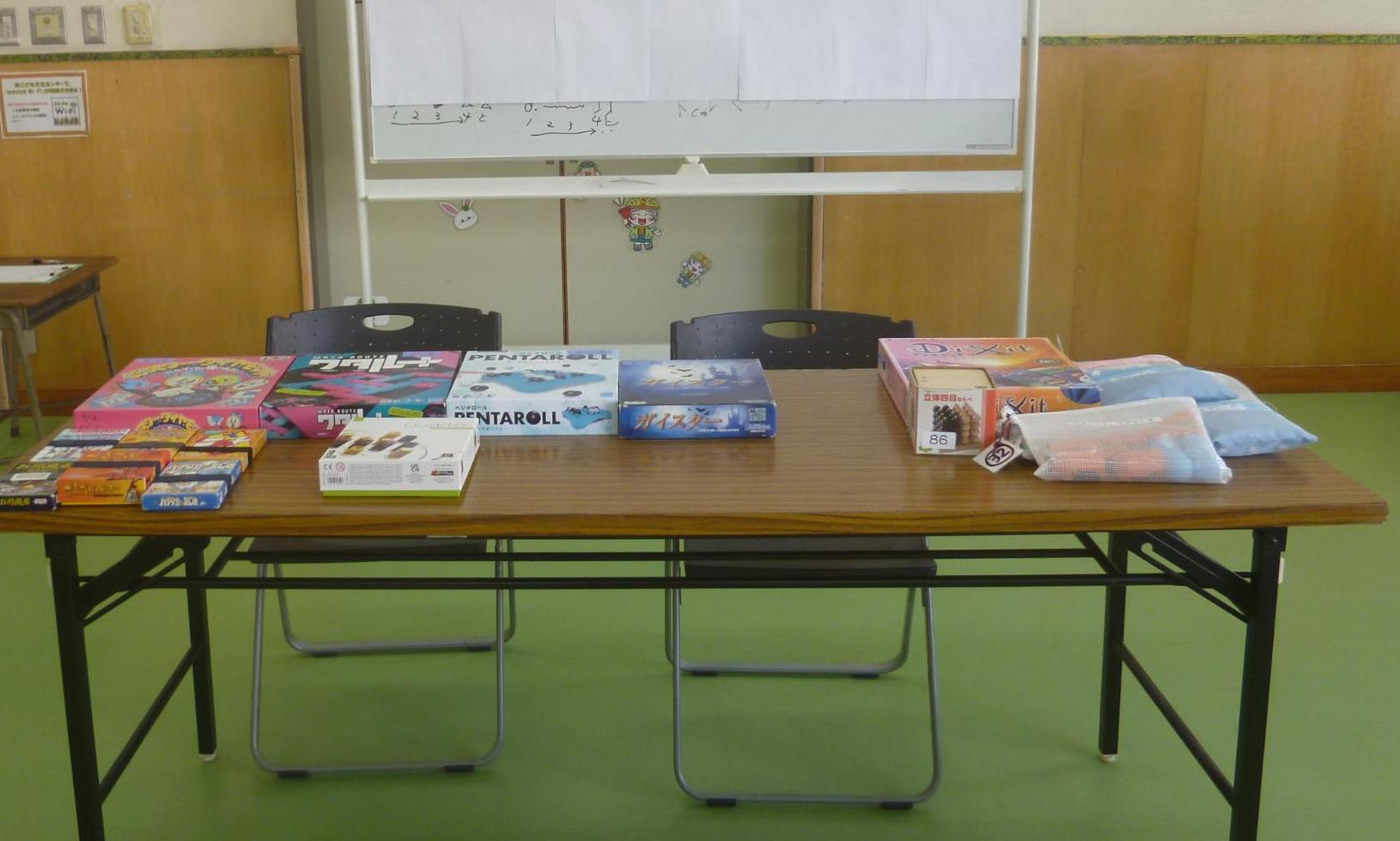 集会室に長机を配置し、その上にボードゲームを並べている。子どもたちが選びやすいようにお品書きをホワイトボードに張り出している様子を映した写真。