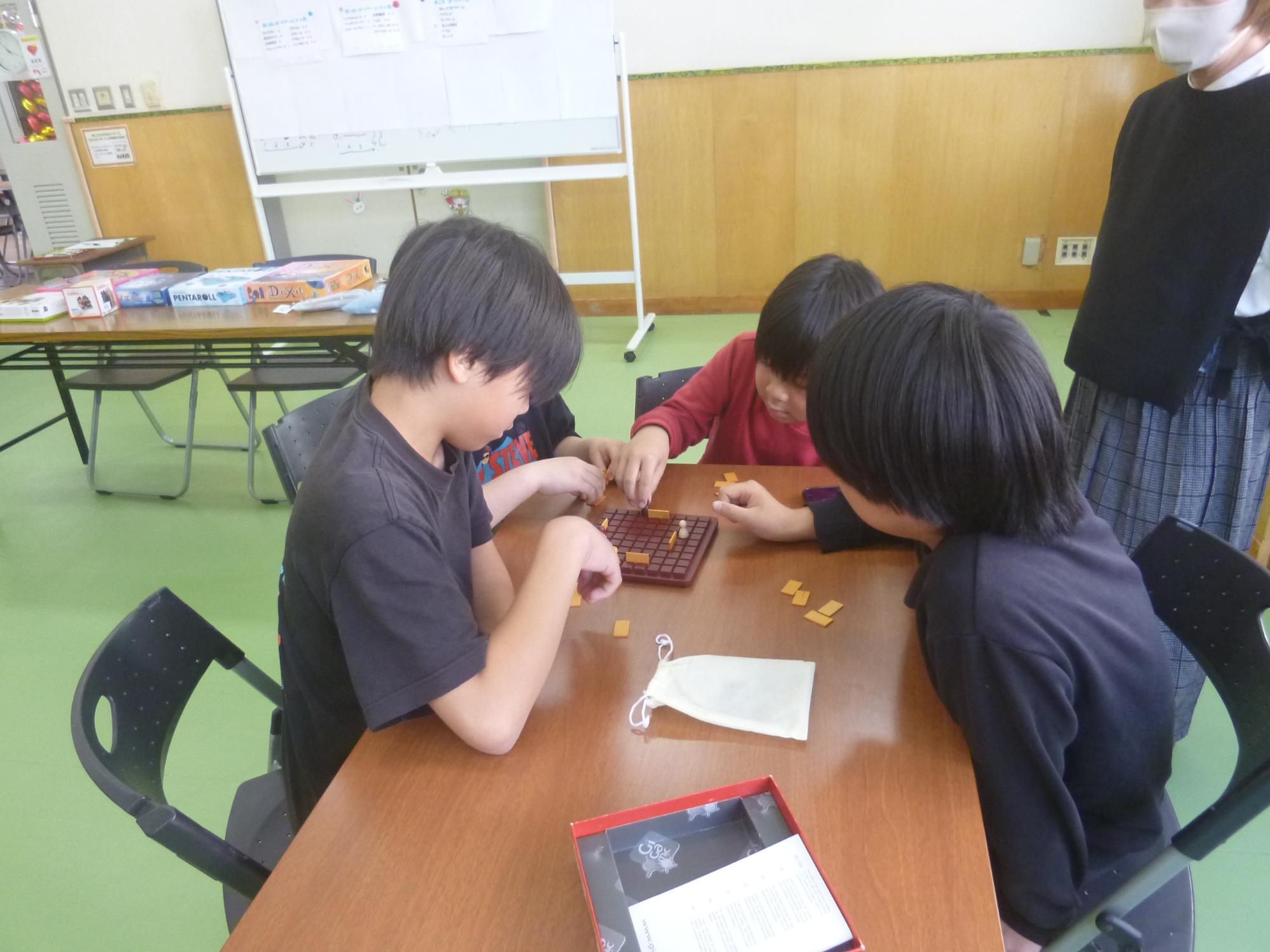 1つのボードゲームを4人で遊ぶ子どもたちの写真。
