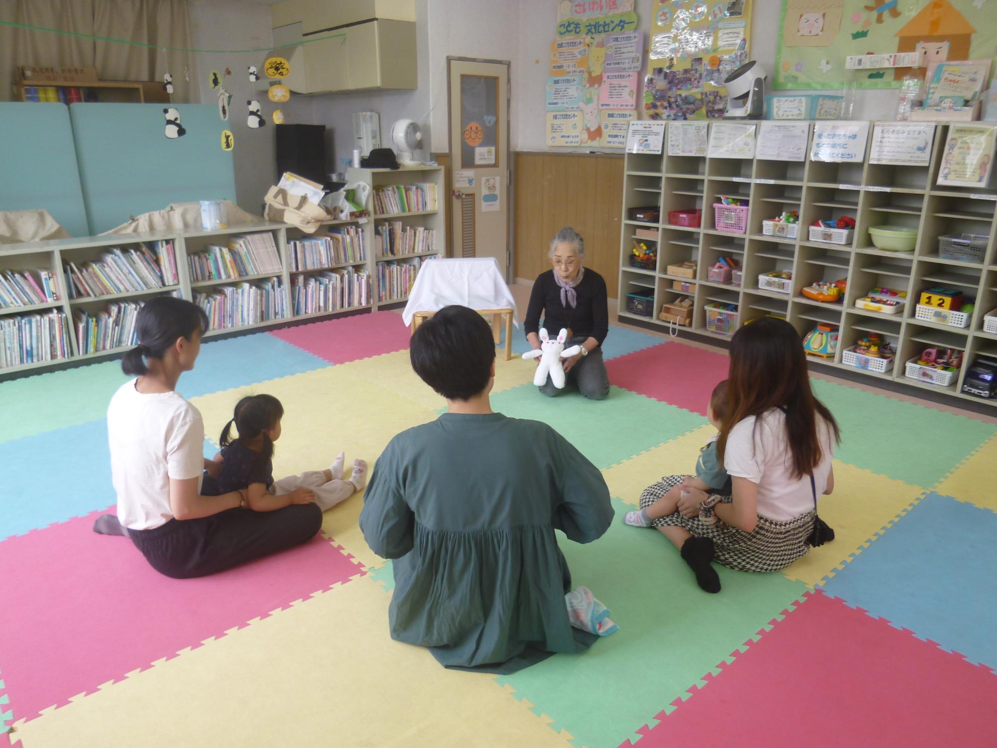 「読み聞かせ＆ちびっこぶんぶん広場」、人形劇の読み聞かせを聞いている幼児親子の写真