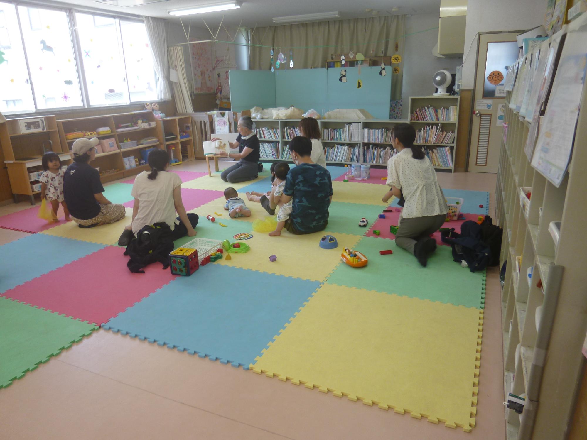 「読み聞かせ＆ちびっこぶんぶん広場」、絵本の読み聞かせを聞いている幼児親子の写真