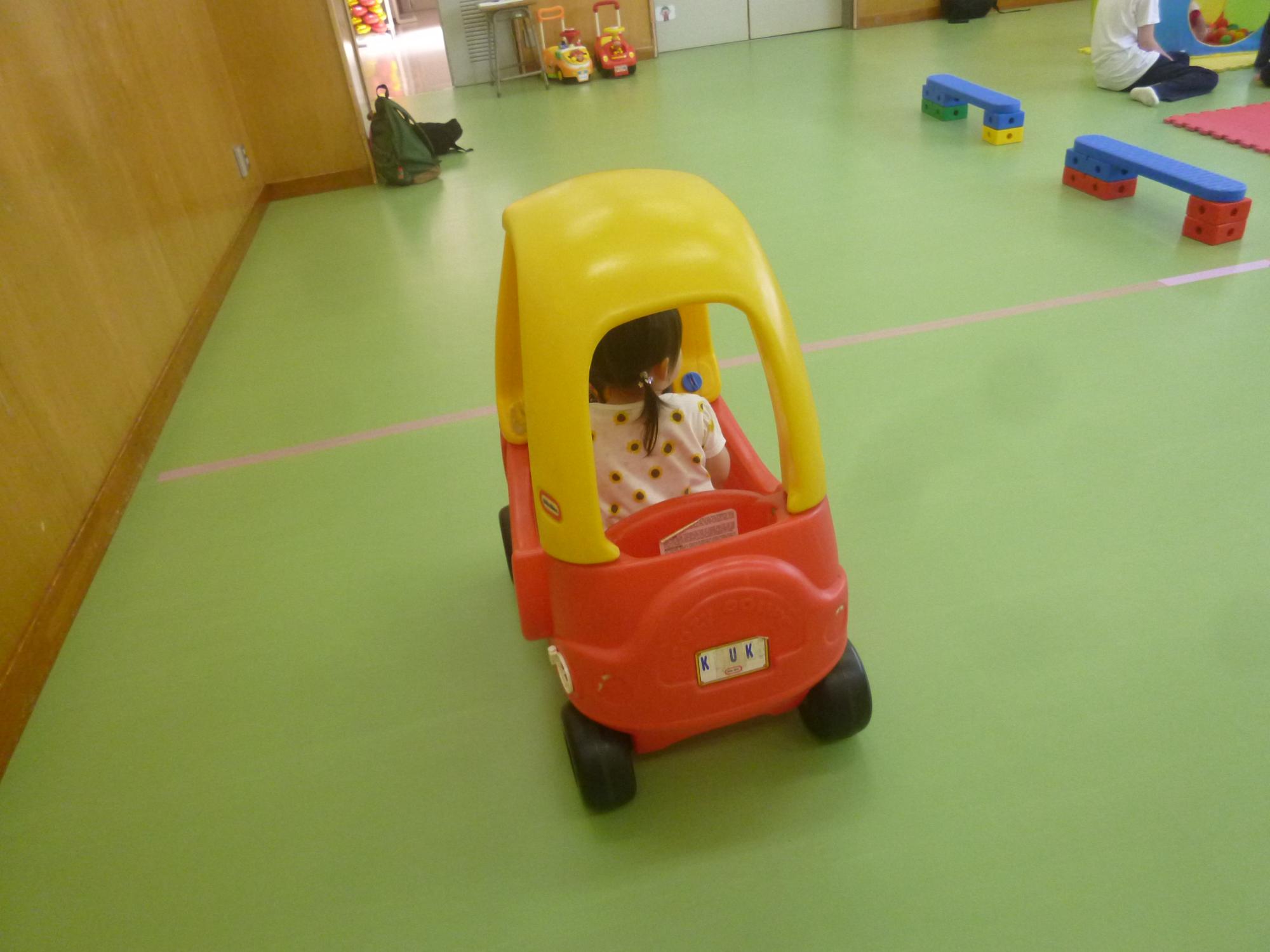 「読み聞かせ＆ちびっこぶんぶん広場」、車のおもちゃに乗って遊ぶ幼児の写真