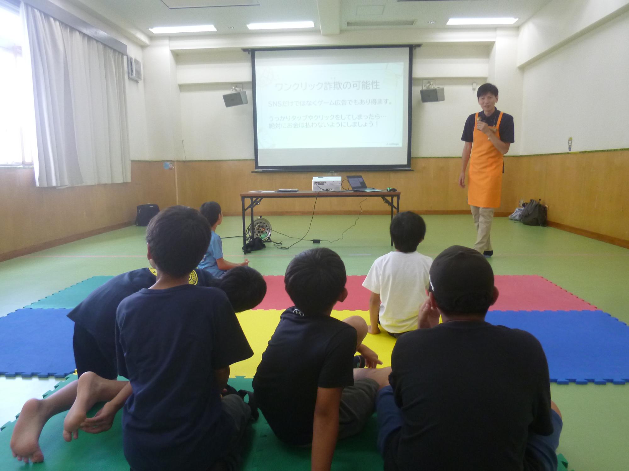 「ITリテラシー講座」集会室でプロジェクターに移された画面を見ながらクイズに答える小学生の写真