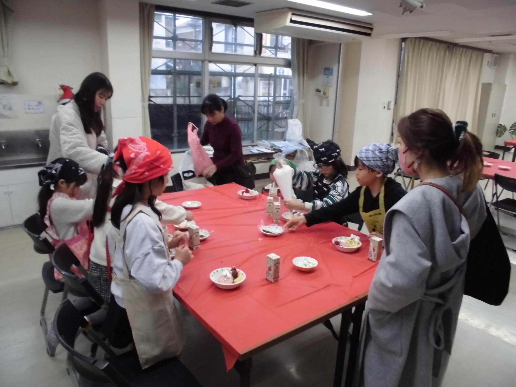 机に赤いテーブルクロスを引いて、ケーキをお皿において、デコレーションをしている様子