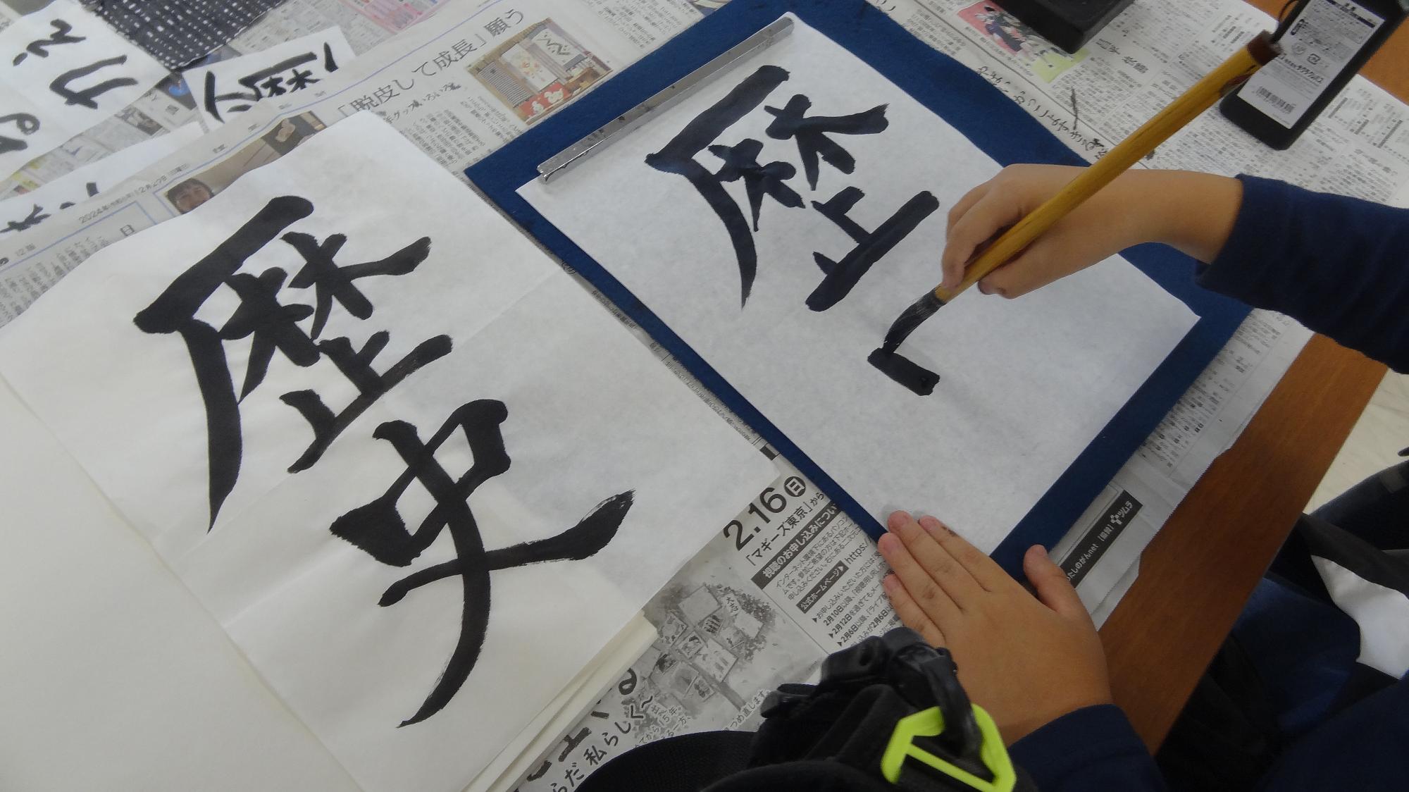 書道の行事で、見本見ながら、歴史という漢字を書いている様子の画像