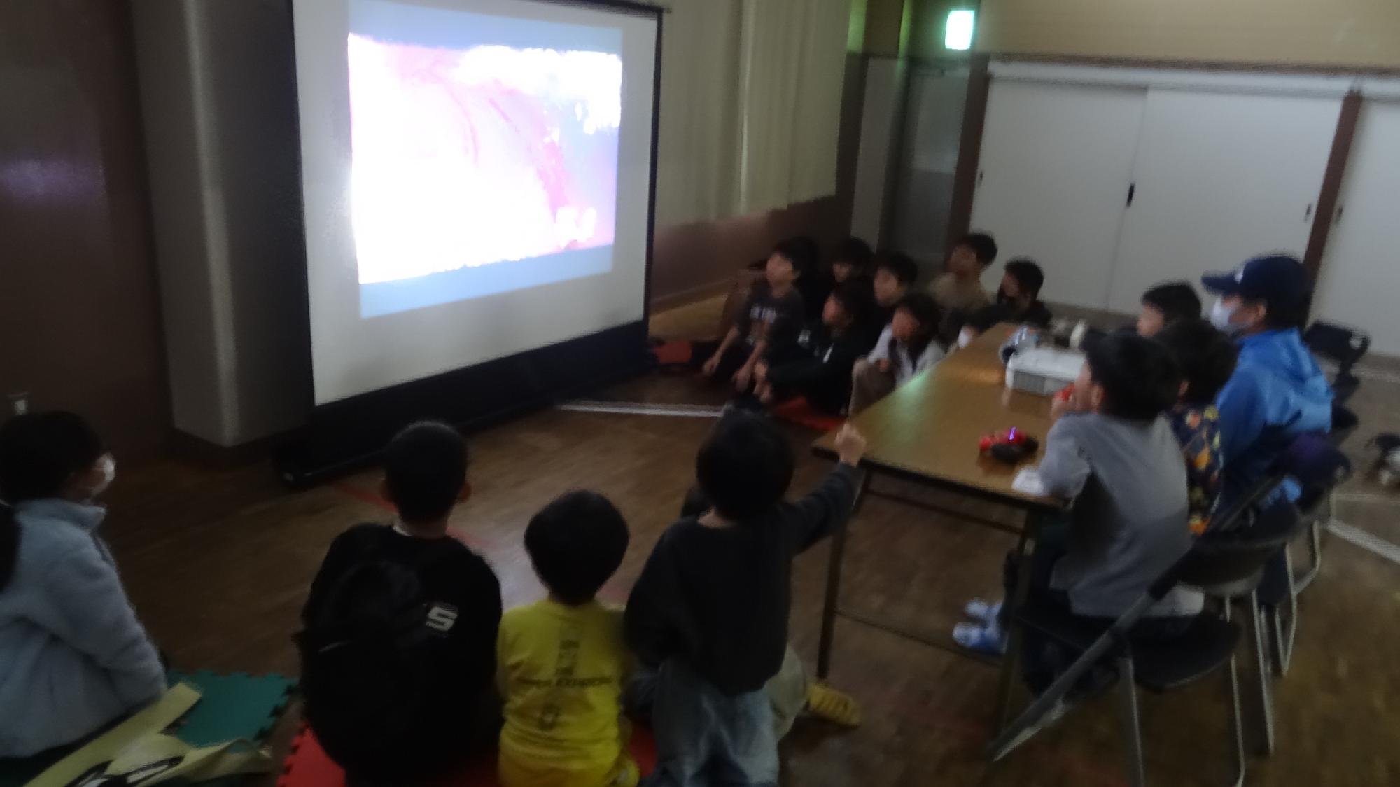 集会室でスクリーンに映像を映して、たくさんのこどもたちが任天堂スイッチをしている様子。
