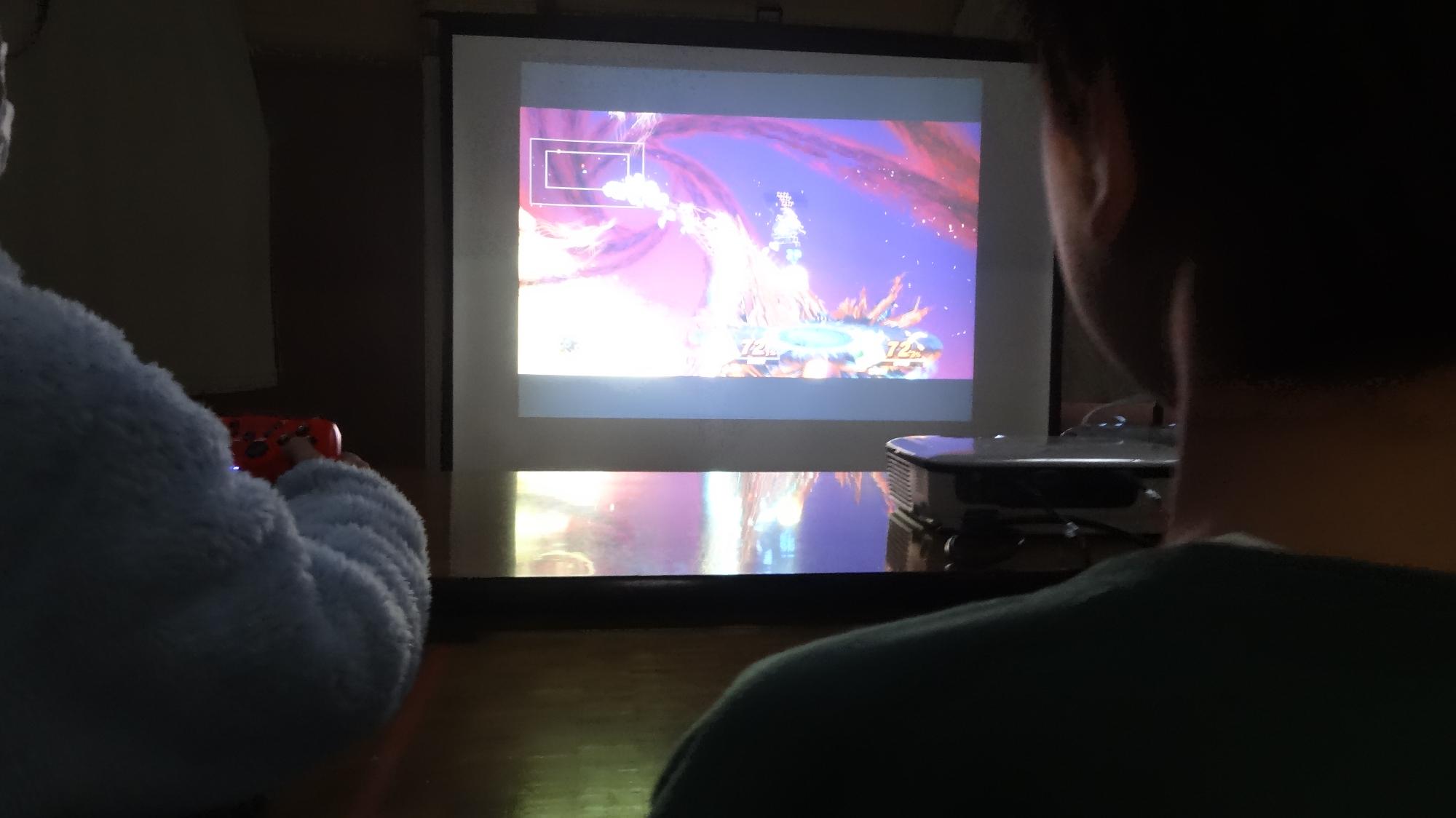 集会室のスクリーンに映像を映して二人の児童が任天堂スイッチをしている様子