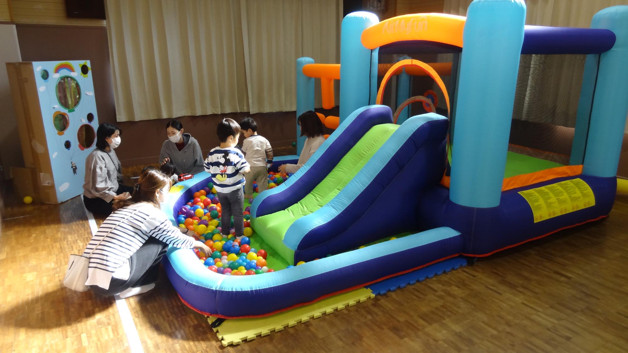 こぶんの集会室にて大きなジャンピングスライダーでこどもたちとその保護者が遊んでいる様子の画像