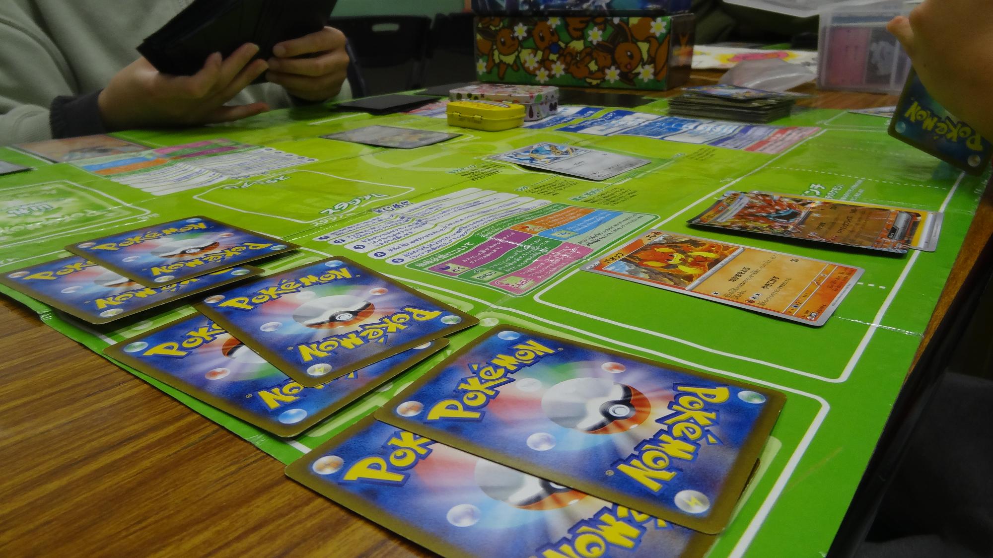 机の上にポケモンカード専用のシートを敷いて、その上にカードを並べてポケモンカードを対戦している様子