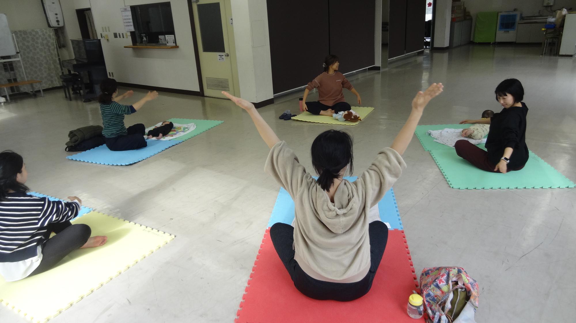 4組の親子が、前にいる先生を見ながらヨガを教わっている様子を後ろから撮った様子の画像