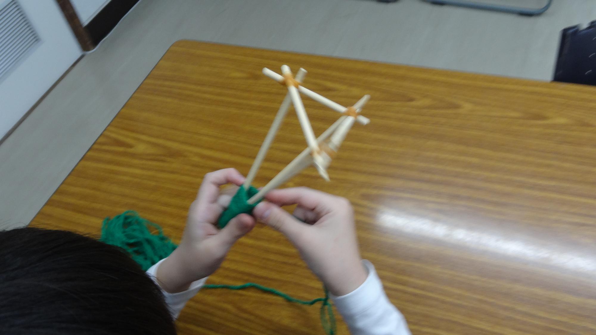 わりばしに緑色の毛糸を巻いている様子