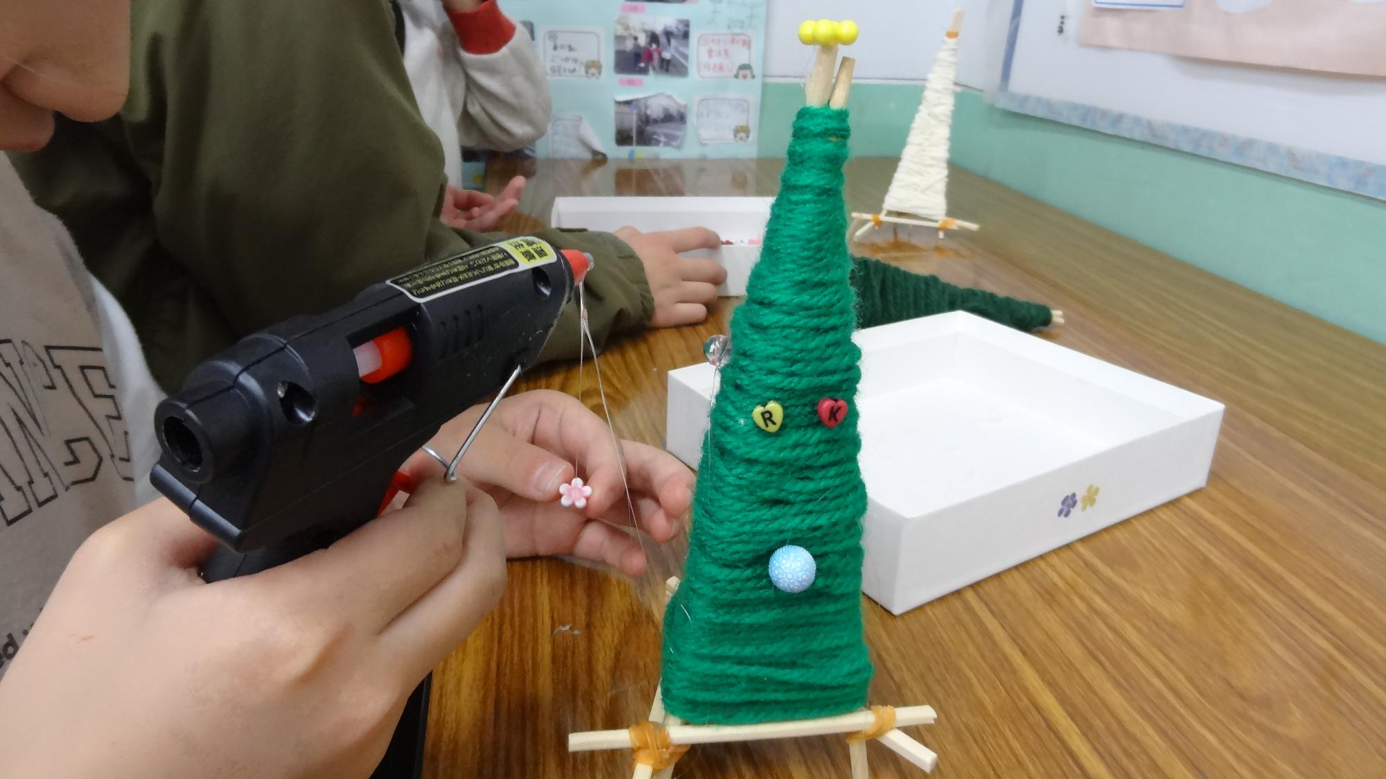 わりばしに巻いた緑色の毛糸にグルーガンでビーズを付けている様子