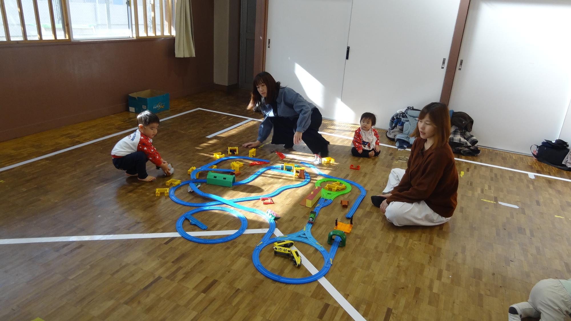幼児親子2組が集会室でプラレールをして遊んでいる様子