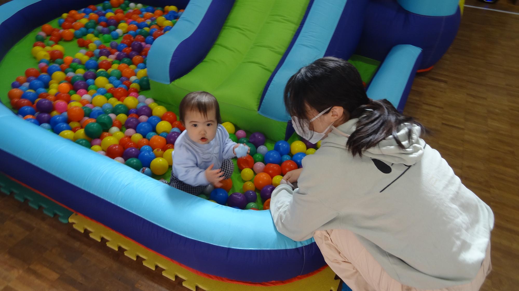 ジャンピングスライダーに敷き詰められたボールに幼児がいる様子。それを保護者が見守っている様子