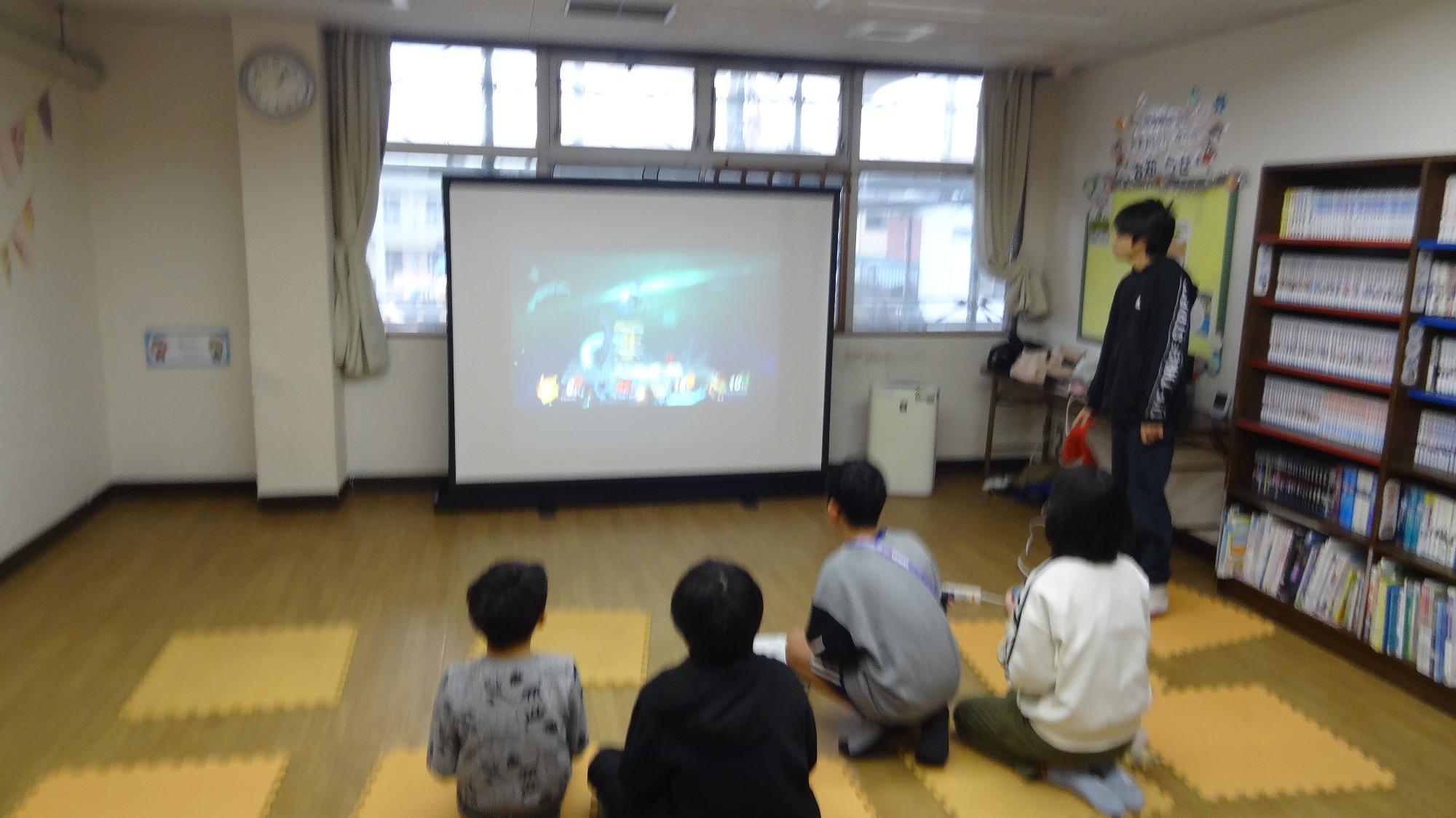 4人の小学生がスクリーンを見ながら大乱闘スマッシュブラザーズをしている様子