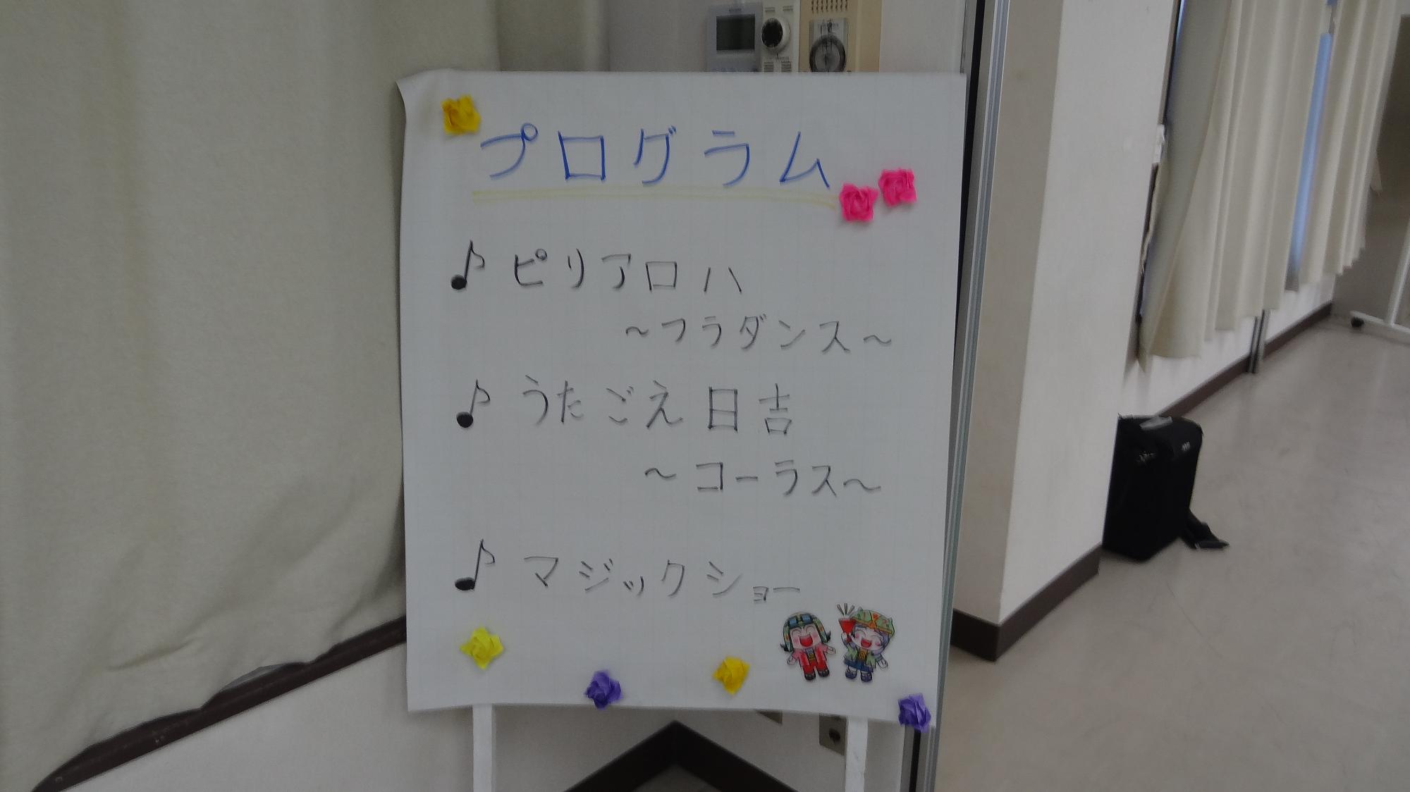 プログラムが書かれた看板、上からピリアロハ～フラダンス～、うたごえ日吉コーラス、マジックショーと書かれている
