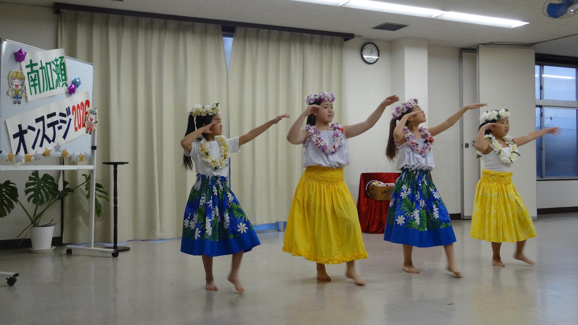 4人が横に並んでフラダンスをしている様子