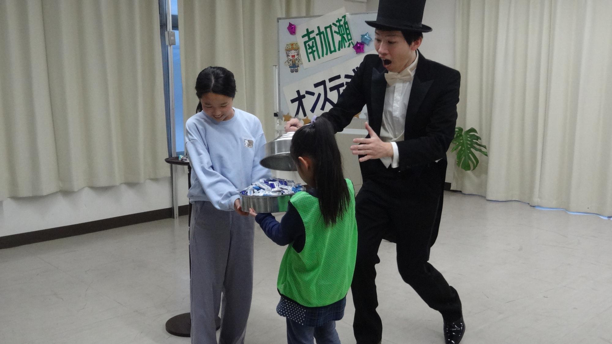 蓋を開けたらお菓子が増えているというマジックに二人の児童が参加している様子