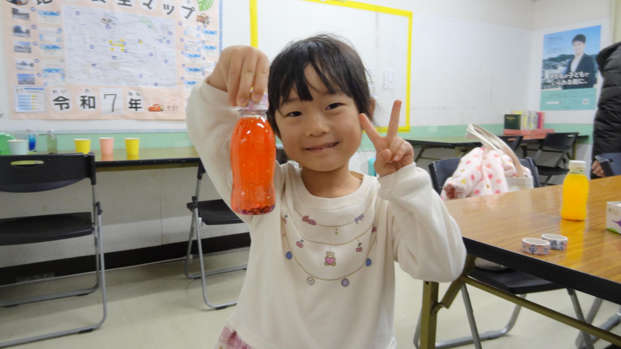 幼児が工作で完成したものを手に持って、ピースをしている様子