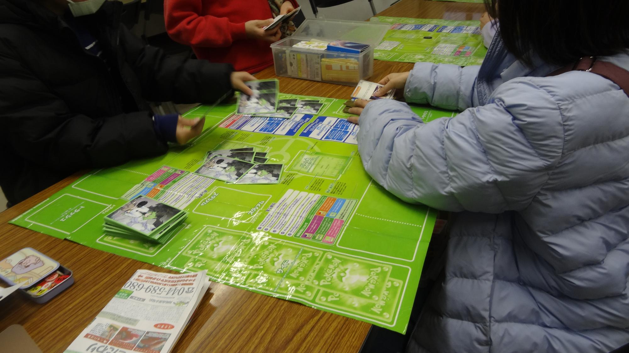 二人の児童が向かい合ってポケモンカードバトルをしている様子