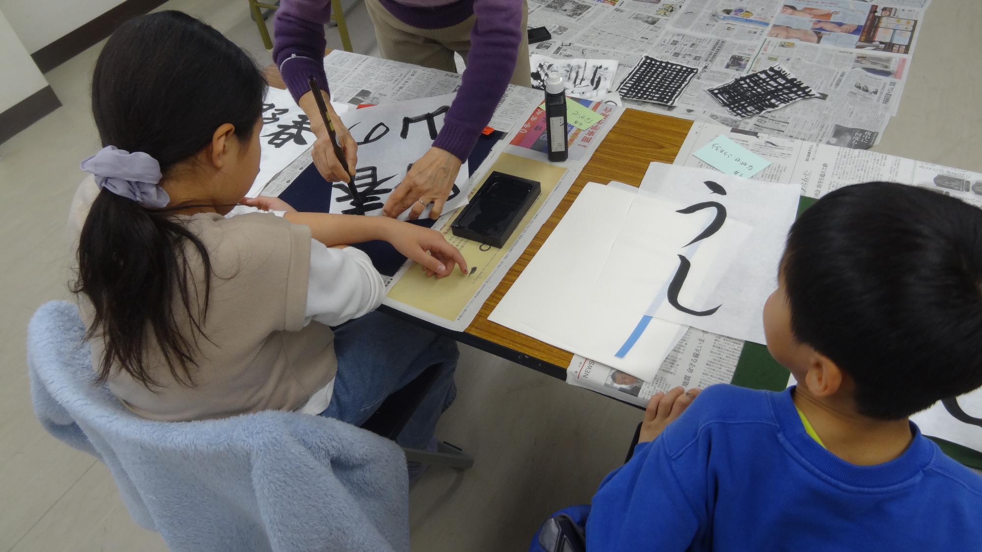 小学生二人が書道をしている様子。右側はうし、左側は春の野山を書いている。